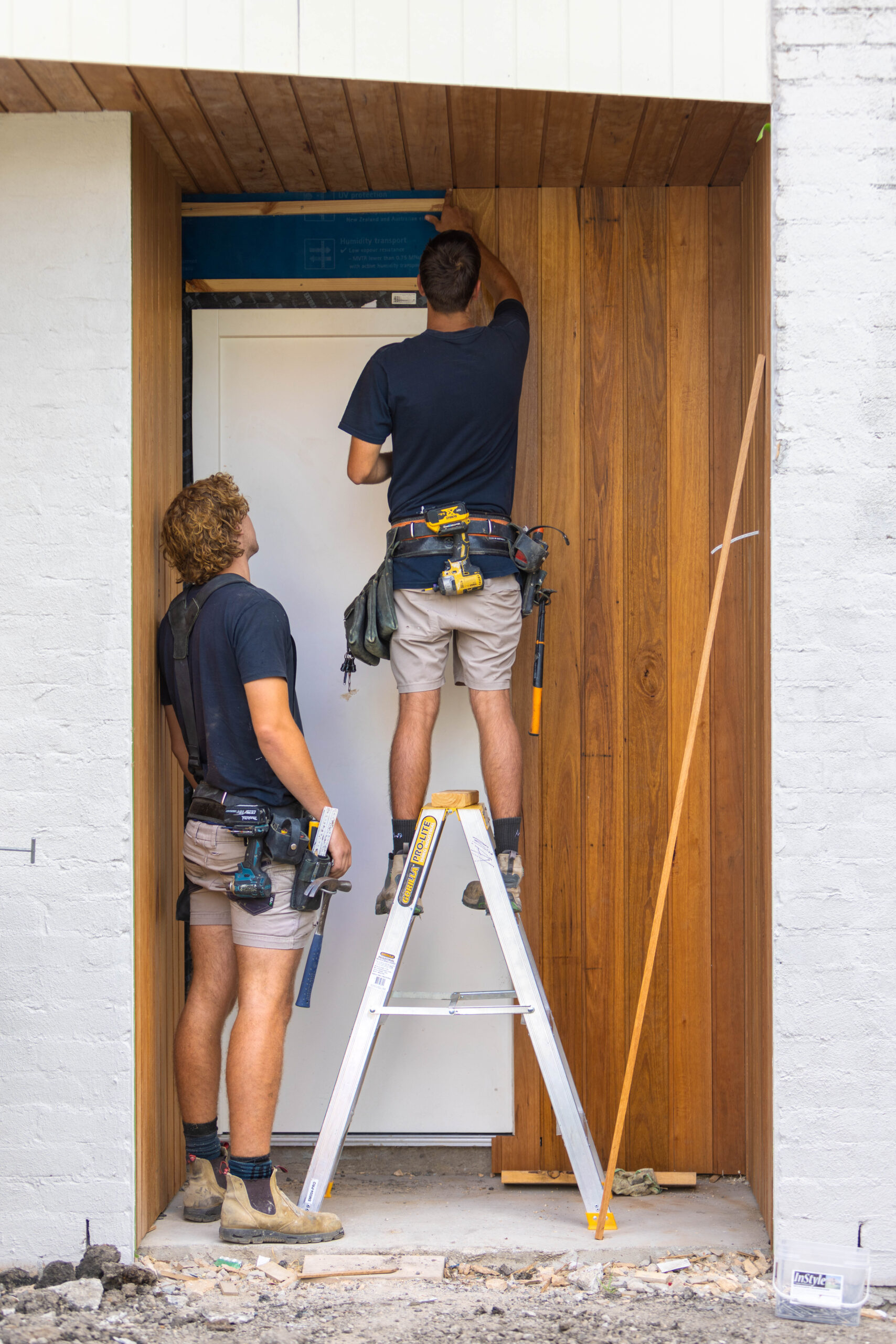 Two tradesmen installing timber cladding to the front entrance of a newly built home in Northcote.
